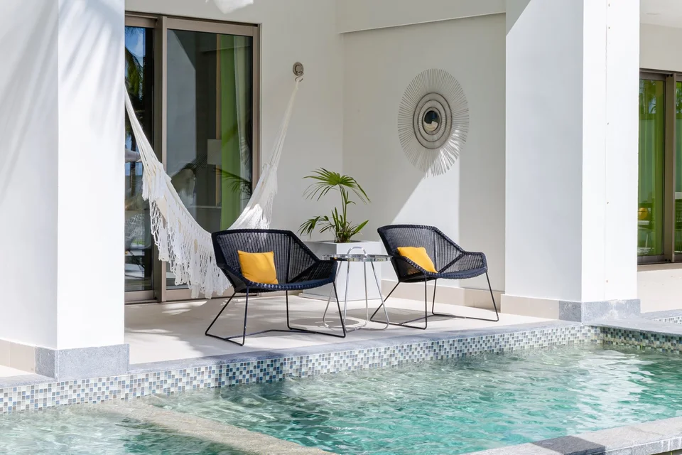 Ground-floor terrace with a white macramé hammock, two black wicker chairs with yellow cushions and a mosaic-edged swim-up pool in front. There is no Jacuzzi and no ocean in frame