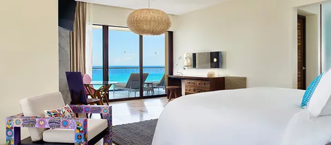 King-bed suite with embroidered painted armchair, purple chair, woven pendant and glass doors to a terrace with sea view. Not an 'Oaxacan Suite' (no such category).