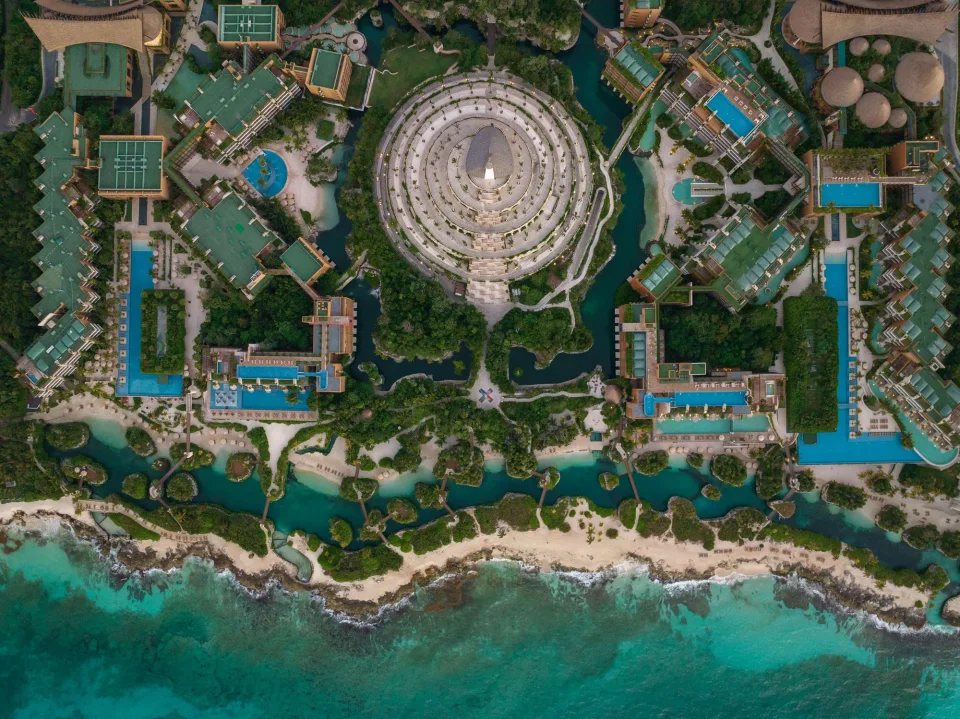 WebP without proper extension: straight-down aerial of the whole complex centred on the circular Xpiral pyramid, with pools, Casas, river channels and the coastline. Likely covers both Xcaret hotels.