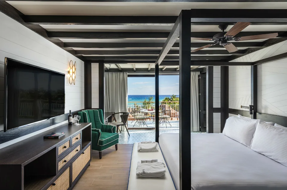 Suite with dark timber beams, a four-poster bed, a green velvet armchair and a balcony with ocean view. This is ORP's renovated suite style, but the exact category is not confirmed (no 'Deluxe Ocean View Suite' category exists).