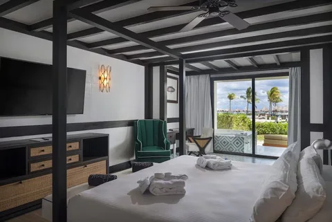 No bunk beds: a four-poster king bed, green armchair and TV, with a ground-floor terrace and tiled outdoor jacuzzi looking towards beach palapas. Consistent with a ground-floor Paradise or Privilege jacuzzi suite; category not confirmed.